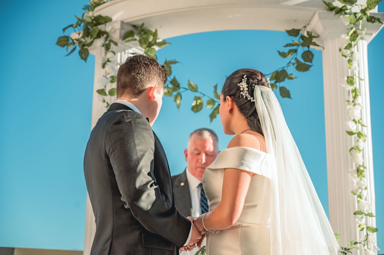 Bride and groom holding hands in an outdoor ceremony under a floral arch.