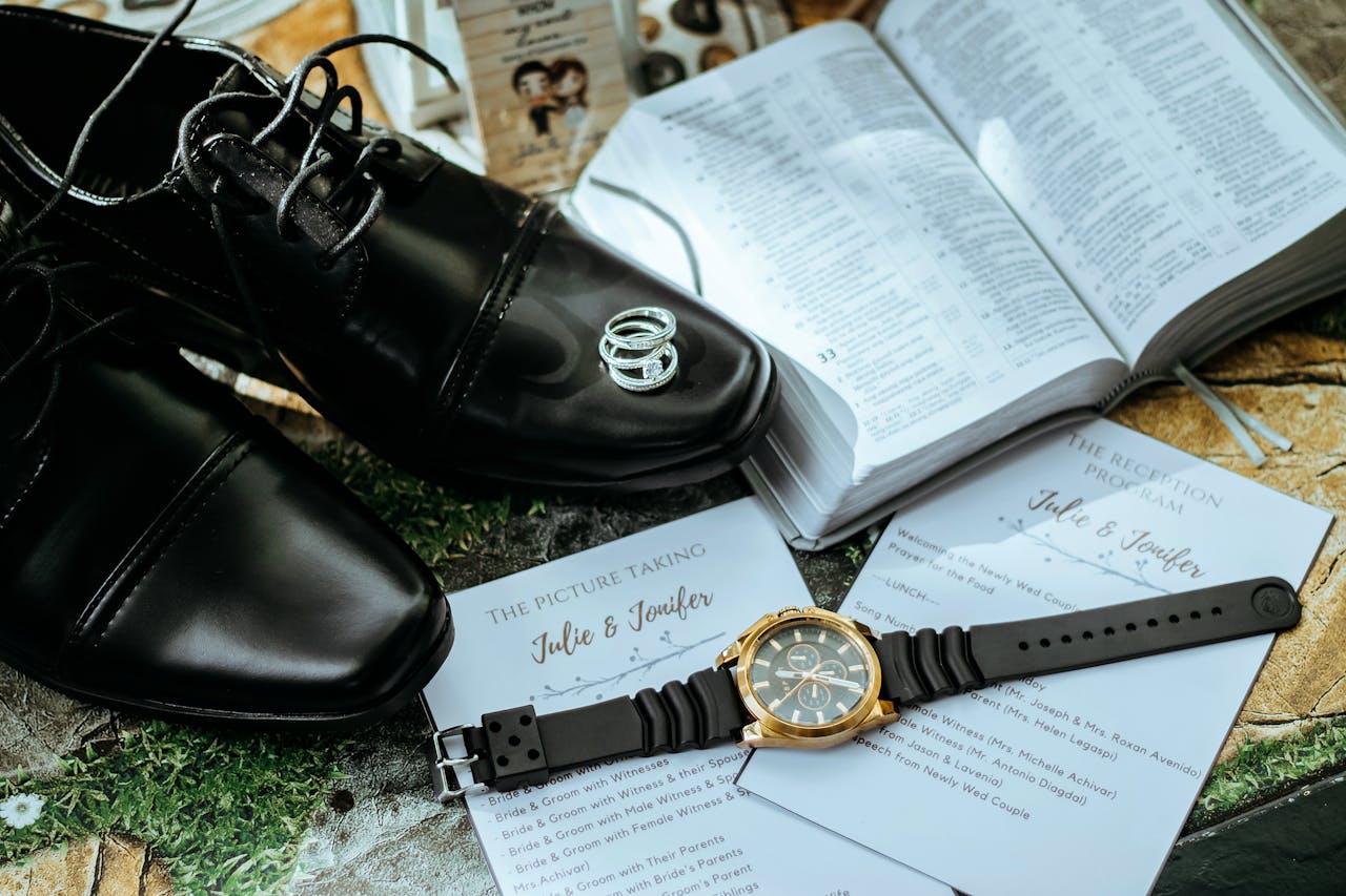 Stylish black shoes with wedding rings, watch, and ceremony programs in an elegant setting.